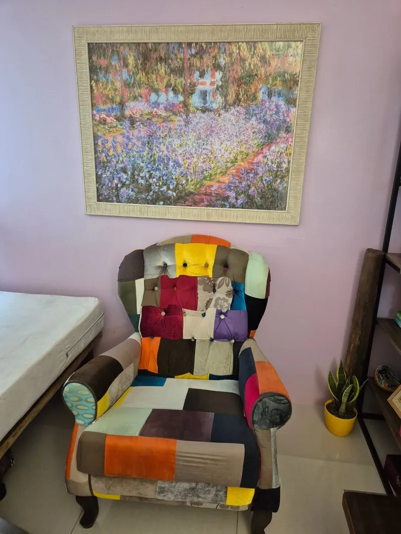 Poltrona de patchwork colorida no consultório, sob um quadro de jardim florido